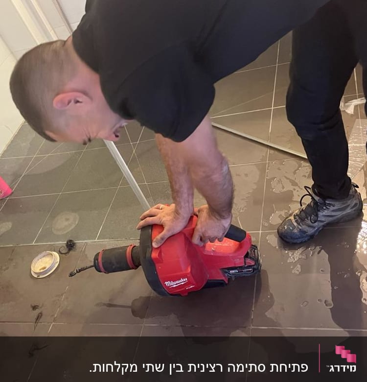 אדם משתמש במקדחה אדומה על רצפת חדר אמבטיה רטובה
